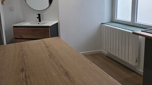A modern bathroom with a wooden vanity, a round mirror, a white sink, and a window with a view.
