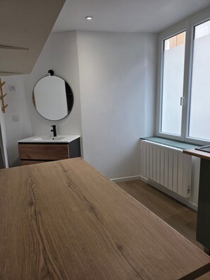 Une salle de bain moderne avec un meuble-lavabo en bois, un miroir rond, un lavabo blanc et une fenêtre donnant sur un beau paysage.