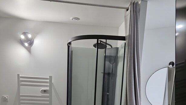 A modern bathroom with a glass shower enclosure, a towel rack, and a wooden floor.