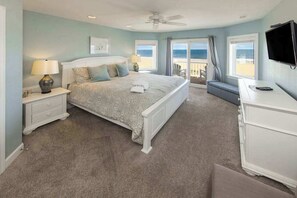 A bedroom with a bed, nightstands, a dresser, a TV, and a balcony with a view of the ocean. - Oceanfront home with private pool, hot tub, outdoor bar, theater room, game room (Virginia Beach)