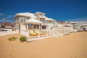 A beachfront property with a large house, a covered deck, and a sandy beach. - Oceanfront home with private pool, hot tub, outdoor bar, theater room, game room (Virginia Beach)