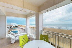 A balcony with a view of the beach, a pool, and a building with multiple levels. - Coastal-themed beachfront condo with water views, W/D, pool, gym & AC (Virginia Beach)