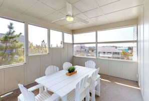 Ein Zimmer mit weißem Tisch, weißen Stühlen, einem Deckenventilator und großen Fenstern mit Blick auf Gebäude und Bäume.