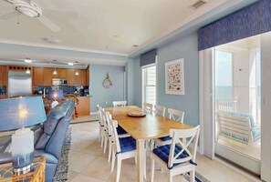 A modern kitchen with wooden cabinets, a dining area with a wooden table and white chairs, and a balcony with a view. - Oceanfront corner condo with amazing balcony views, outdoor pool & gym (Virginia Beach)