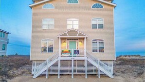 A two-story beach house with a front porch, a staircase, and a beach view. - Spacious beach house with indoor pool, hot tub, & multiple decks (Virginia Beach)