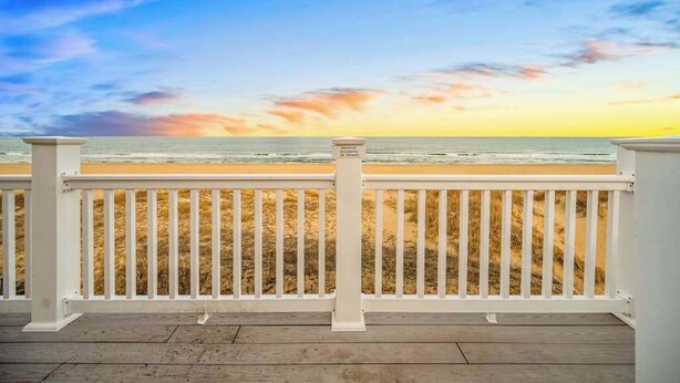 A wooden deck with white railings overlooking a beach. - Spacious beach house with indoor pool, hot tub, & multiple decks (Virginia Beach)