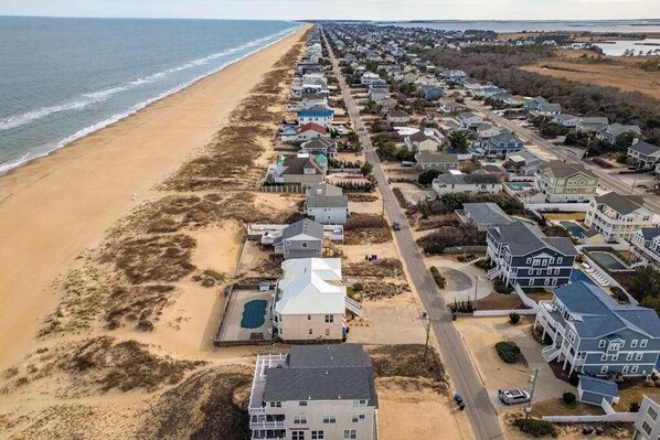 A coastal residential area with houses aligned along a beach, featuring a mix of single and multi-story buildings, roads, and a visible swimming pool. - Spacious beach house with indoor pool, hot tub, & multiple decks (Virginia Beach)