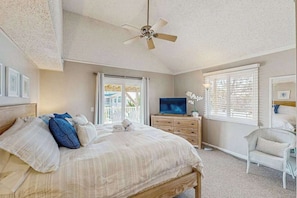 Ein Schlafzimmer mit Bett, Deckenventilator, Fernseher, Kommode und Fenster mit Jalousien.