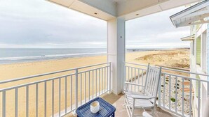 Ein Balkon mit Blick auf Strand und Steg, weiße Stühle und ein kleiner Tisch mit einer Tasse.