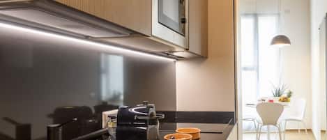 A modern kitchen with a built-in oven, a coffee machine, and a dining area with a white table and chairs.