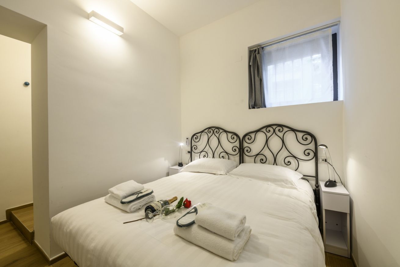 Una cama bien hecha con sábanas blancas, una lámpara de noche y una mesita con una botella y un vaso.