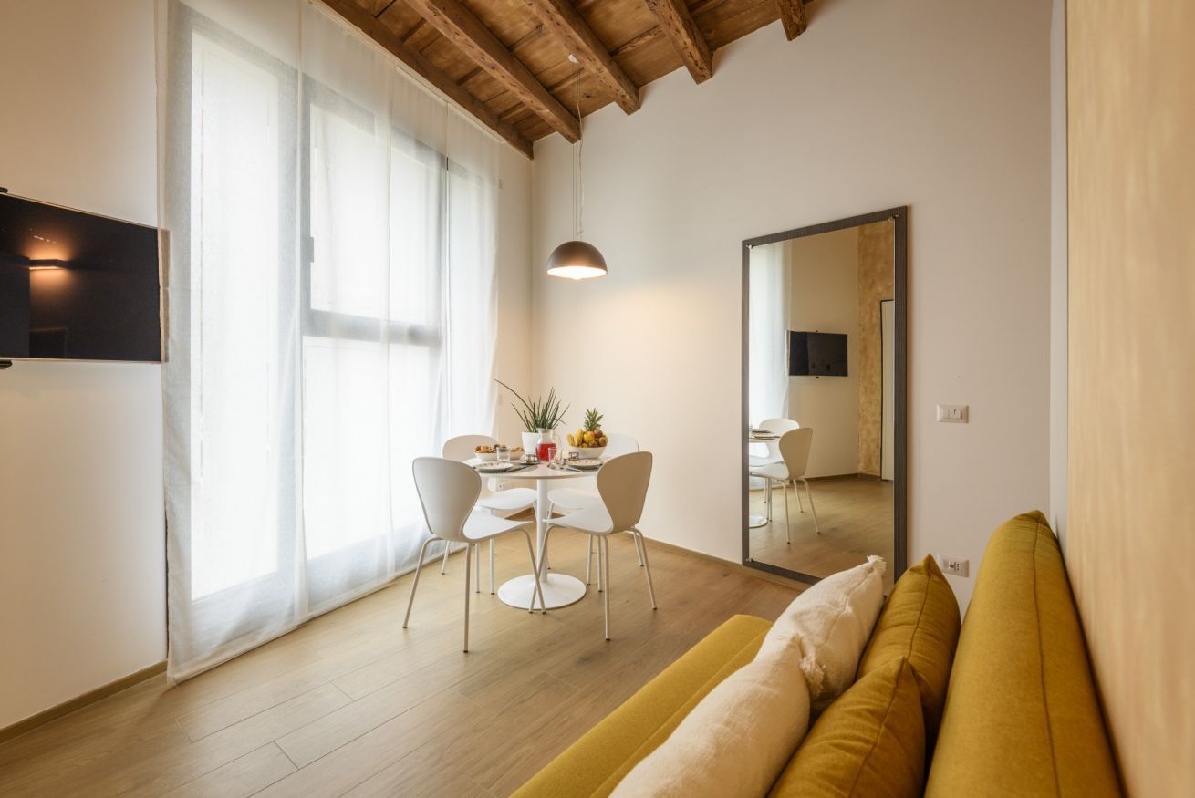 Ein modernes Wohnzimmer mit Holzboden, einer Couch, einem Esstisch mit Stühlen und einem großen Spiegel.