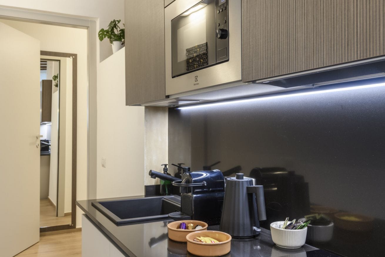 Een moderne keuken met een magnetron, koffiezetapparaat en een klein plantje op het aanrecht.