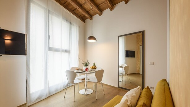 En moderne stue med træloft, sofa, spisebord med stole og et stort spejl.