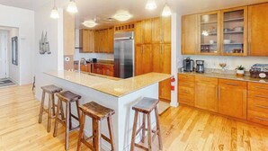 A modern kitchen with wooden cabinets, a central island with stools, stainless steel appliances, and pendant lighting. - Two-story penthouse with huge bay views & pools - steps to beach (Virginia Beach)