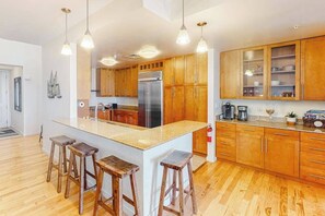 A modern kitchen with wooden cabinets, a central island with stools, stainless steel appliances, and pendant lighting. - Two-story penthouse with huge bay views & pools - steps to beach (Virginia Beach)
