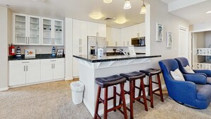 Une cuisine moderne avec des meubles blancs, un îlot central doté de tabourets et un éclairage suspendu.