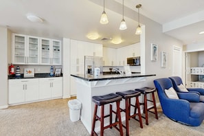 A modern kitchen with white cabinets, a central island with stools, and pendant lighting. - Top-floor corner courtyard home with pool, gym, & game system (Virginia Beach)