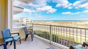 A balcony with chairs, a view of the beach, and a house in the background. - Oceanfront condo w/incredible beach views, shared outdoor pool, gym, & A/C (Virginia Beach)