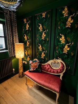 A room with a green wall, a red upholstered bench, a gold-framed mirror, and a patterned lamp. - Muddy Boots-La Petite Mews (Kirkby Stephen)