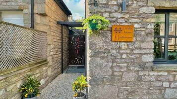 A stone building with a sign indicating 'La Petite Mews' and a number '1'. There are two potted plants in front.
