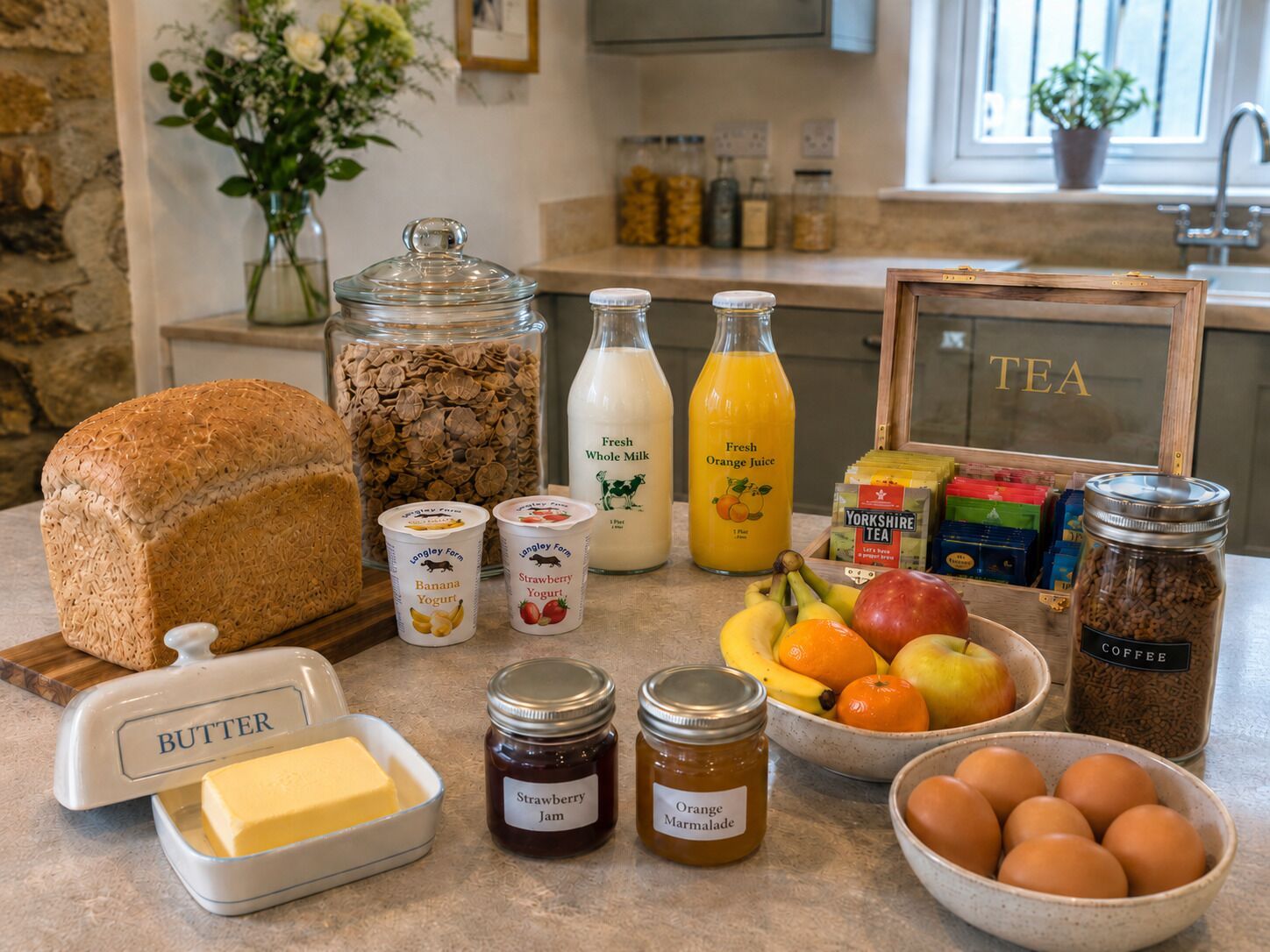 En køkkenbordplade med forskellige madvarer og ingredienser, herunder syltetøjsglas, juiceflasker, et brød og en skål med æg.