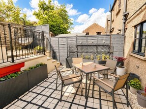 Une terrasse avec une table et des chaises, un petit jardin avec des plantes et une clôture grise.