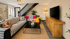 Ein modernes Wohnzimmer mit einer schwarzen Couch, einem Couchtisch, einem Fernseher und einer Treppe.