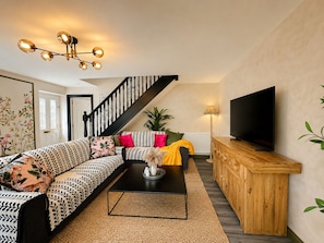 Ein modernes Wohnzimmer mit einer schwarzen Couch, einem Couchtisch, einem Fernseher und einer Treppe.