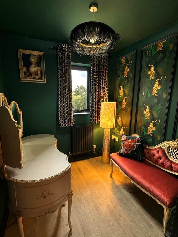 Une pièce avec un fauteuil ancien, un canapé rouge, une lampe sur pied et une fenêtre avec des rideaux.