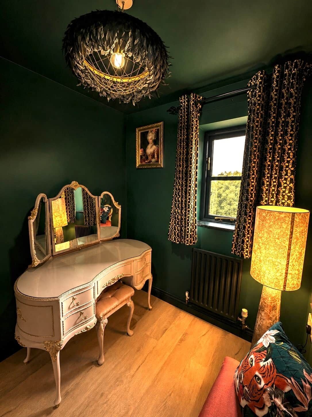 Quarto com toucador antigo, espelho, janela com cortinas estampadas, luminária e almofada com tema de tigre.