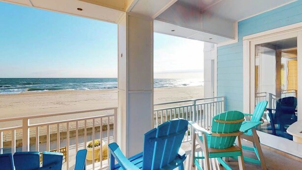 A balcony with a view of the beach, blue chairs, and a table. - Beachfront condo with 2 oceanfront balconies, W/D, pool, & gym (Virginia Beach)