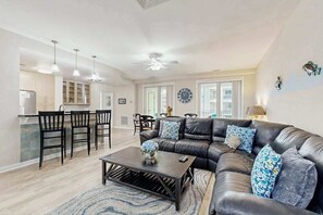 Ein modernes Wohnzimmer mit einer Ledersofa, einem Couchtisch und einem Essbereich mit Stühlen, im Hintergrund eine Küche.
