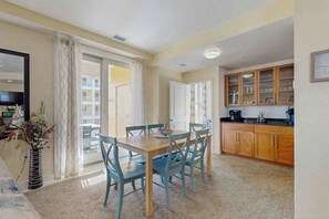 Un coin repas avec une table et des chaises, une cuisine avec des meubles en bois et une vue à travers une porte vitrée.