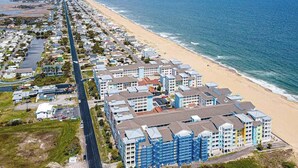 A coastal residential area with beachfront properties, a long road parallel to the beach, and a clear view of the ocean. - Comfortably furnished condo with glimpses of Back Bay, pool & gym (Virginia Beach)