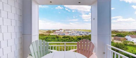 Een balkon met een tafel en stoelen, uitzicht op een parkeerplaats en gebouwen, en een heldere lucht.