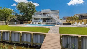 Un edificio de dos plantas con piscina, terraza de madera y asientos al aire libre.