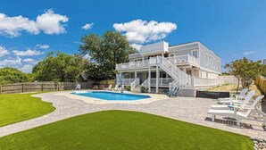 Una casa de dos pisos con piscina, patio cubierto y jardín cercado.