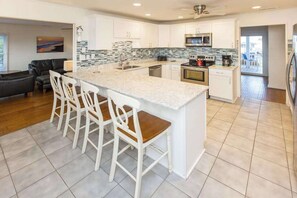 A modern kitchen with a large island, white cabinetry, and a tiled backsplash. - Lovely canal-front home between bay & beach with private pool, dock, & AC (Virginia Beach)