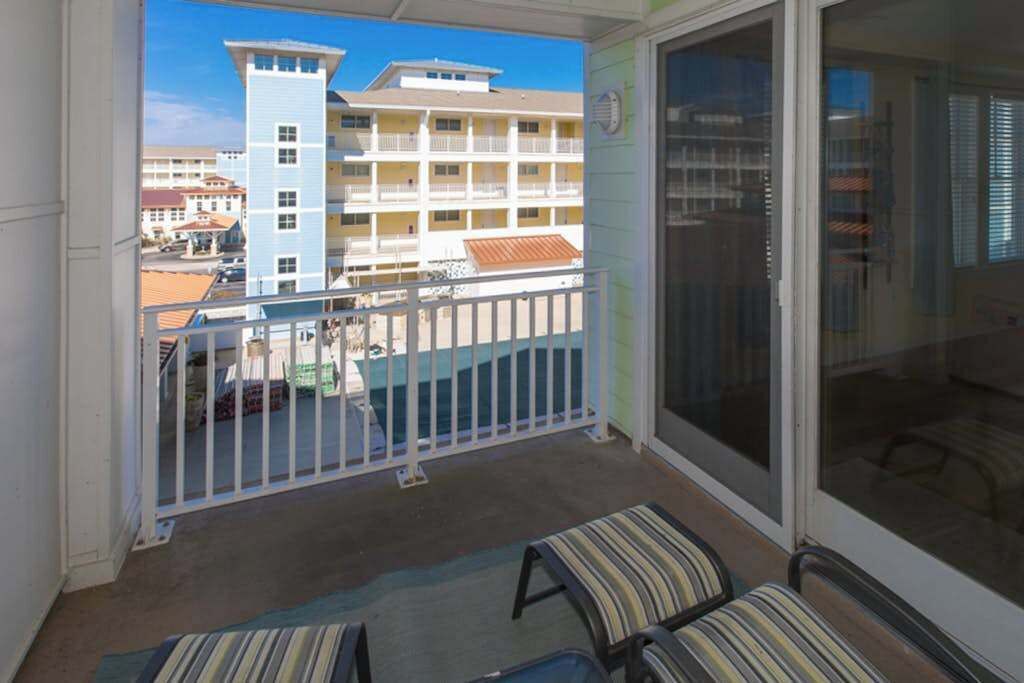 A balcony with a view of a building complex, a sliding glass door, and two striped chairs.