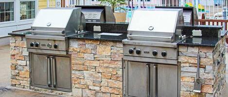 A stone-built outdoor grill station with two gas grills, a control panel, and a stainless steel cabinet.