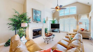 A living room with a fireplace, a television, a ceiling fan, and a large window with blinds. - Fantastic oceanfront home w/private pool & hot tub, WiFi, central AC, & deck (Virginia Beach)