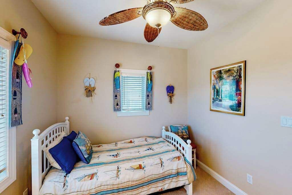 A bedroom with a bed, a ceiling fan, a window with blinds, wall art, and a door with hanging items.