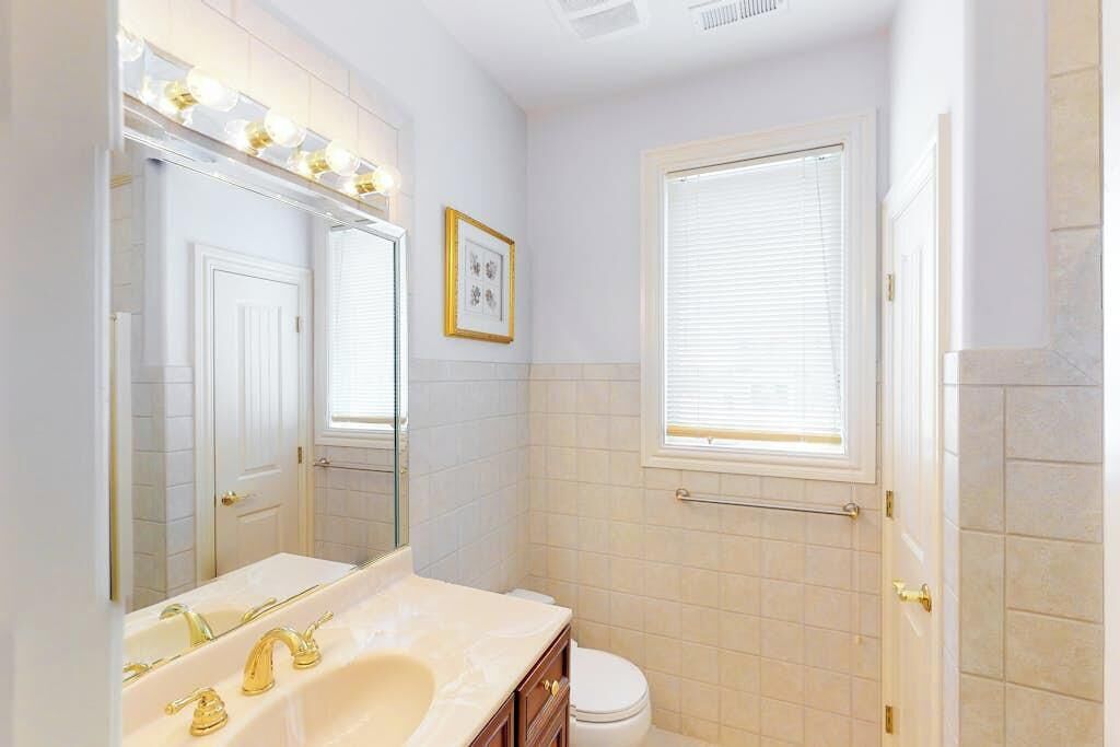 Une salle de bain avec un lavabo blanc, des robinets dorés, des toilettes blanches et une fenêtre avec des stores.