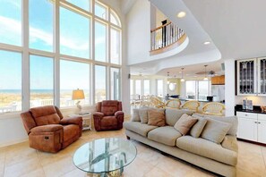 A spacious living area with large windows, a curved staircase, a glass coffee table, and a beige sofa. - Amazing beachfront house w/private washer/dryer, WiFi, central AC, Ping-Pong (Virginia Beach)