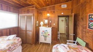 Ein Zimmer mit Holzwänden, zwei Betten mit gemusterten Bettbezügen, eine Kommode mit floralem Dekor und einem Spiegel.