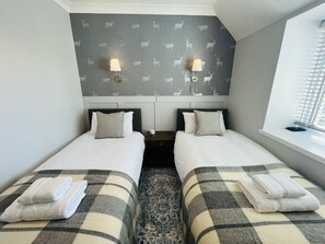 Ein Doppelzimmer mit zwei Betten, einem gemusterten Wandteppich, Nachttischlampen und einem Fenster mit Jalousien.