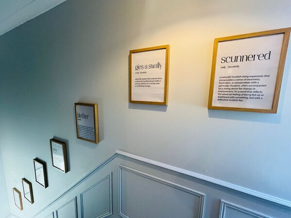 A hallway with framed signs on the wall, including 'gies a swally' and 'scunnered'.