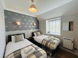 A bedroom with two beds, a window with blinds, a radiator, and a wall with a deer pattern.