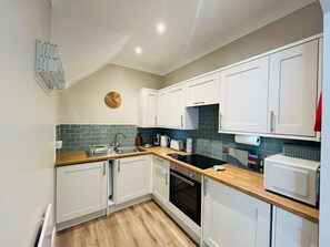 A kitchen with white cabinets, a wooden countertop, a microwave, a toaster, and a clock on the wall.